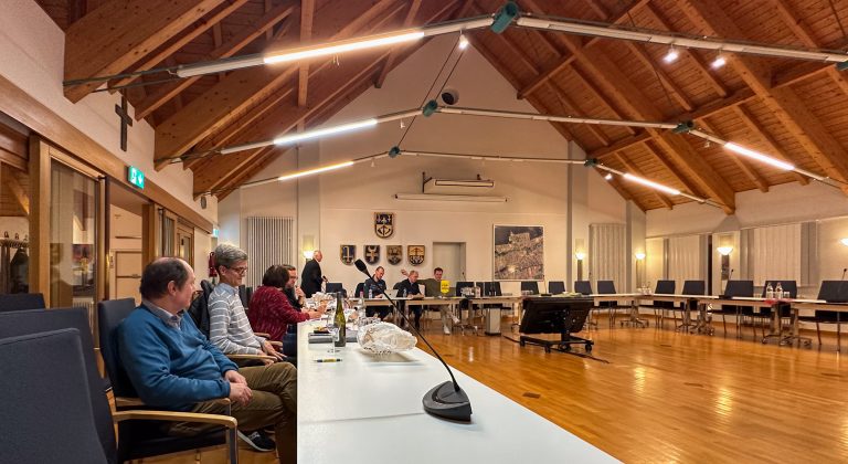 Versammlungssaal mit Personen und Wappen.